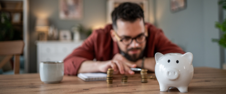 Renter sitting at a table comparing stacks of coins next to a piggy bank, tracking savings and monthly expenses for apartment budgeting.