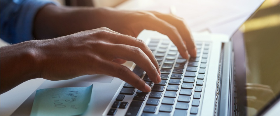 Close-up of a person's hands writing something on a laptop's keyboard to illustrate completing a lease renewal outside peak season.