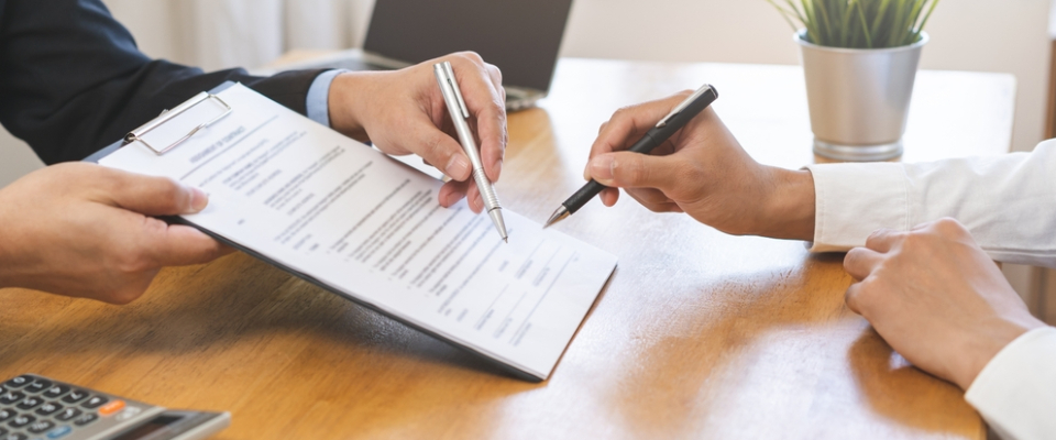 Landlord and renter reviewing and signing a lease extension agreement at a desk, pointing to terms on the document before finalizing the updated rental contract.