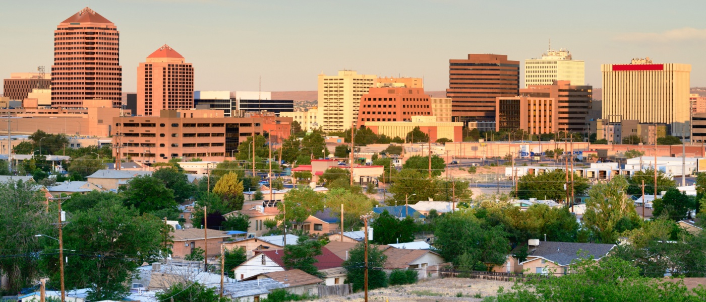 New apartments in Albuquerque highlighted by the downtown skyline at dawn, with city buildings under soft morning light.