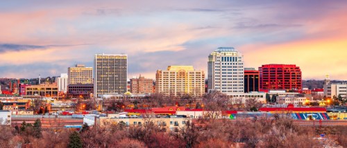 New apartments in Colorado Springs highlighted by the downtown skyline at dawn, with city buildings under soft morning light and mountain views nearby.
