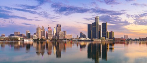 New apartments in Detroit highlighted by the skyline at dawn along the Detroit River, featuring modern buildings in soft morning light.