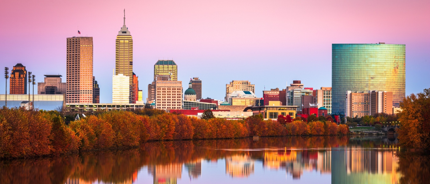 New apartments in Indianapolis highlighted by the city skyline along the White River at dusk, with modern buildings and soft evening light.