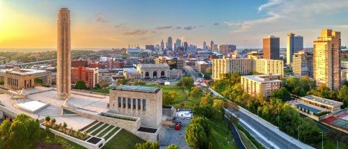 New apartments in Kansas City highlighted by the downtown skyline at dusk, with city lights illuminating the urban landscape.