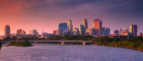 New apartments in Minneapolis highlighted by a panoramic autumn sunrise over the downtown skyline, with colorful foliage and city buildings in view.