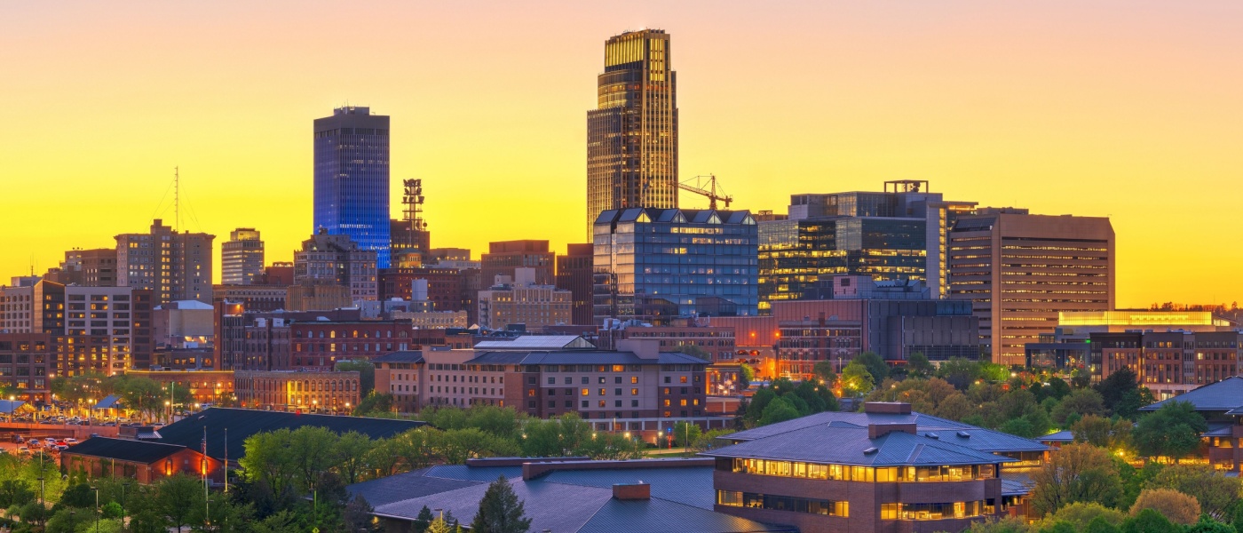 New apartments in Omaha highlighted by the downtown cityscape at dusk, with illuminated buildings and evening sky over the urban core.