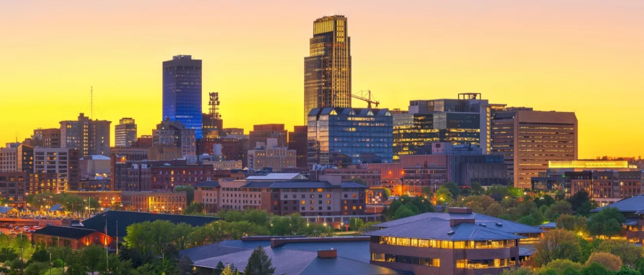 New apartments in Omaha highlighted by the downtown cityscape at dusk, with illuminated buildings and evening sky over the urban core.