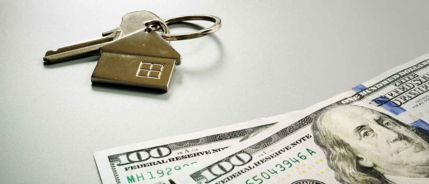 House-shaped keychain and apartment keys placed next to U.S. dollar bills, symbolizing rent collection, monthly rent payments and the cost of renting an apartment.