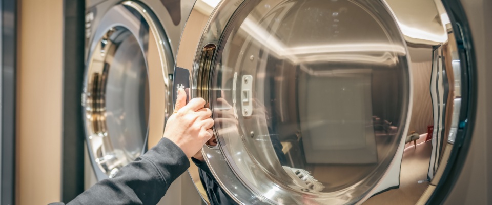 Close-up of a resident wiping down the door of a stainless steel dryer in a shared laundry room after finishing a load.