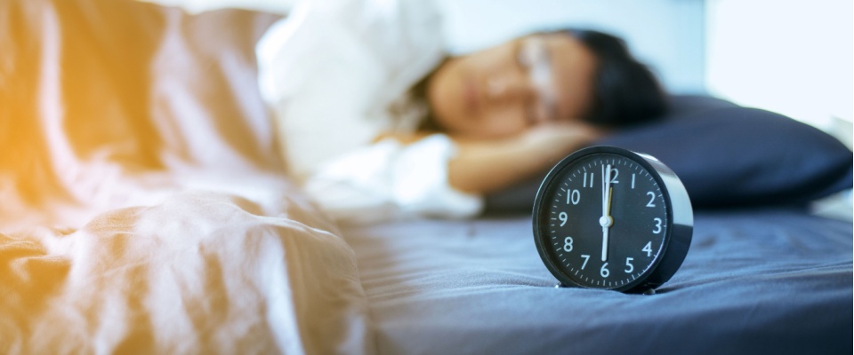 A woman sleeping with an alarm clock on the bed in front of her.