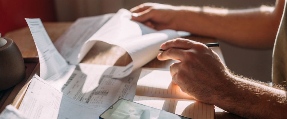 Close-up of hands using a calculator while reviewing multiple utility bills and notes, representing expense tracking and documentation like a rent receipt.