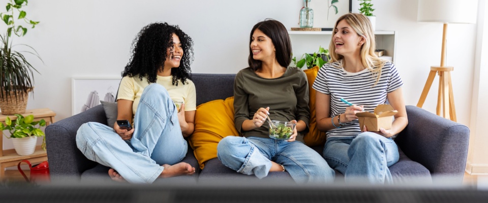 Three college roommates gathered around a laptop in a shared apartment, reviewing information together like co-applicants preparing a rental application.