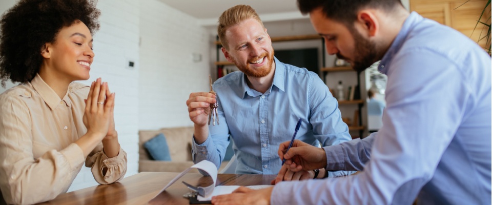 Three people around a table signing a document and holding a set of keys to illustrate an apartment cosigner versus a coapplicant and the main differences.