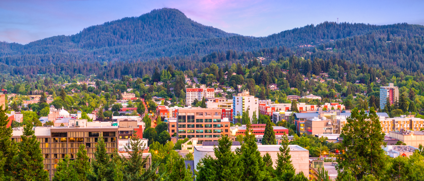 Downtown Eugene, Oregon with mid-rise apartment buildings, tree-lined streets and forested hills in the background, showcasing affordable neighborhoods with budget-friendly rentals and scenic surroundings.