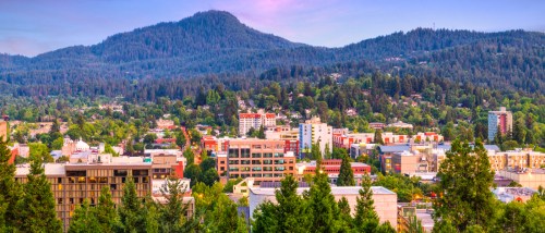 Downtown Eugene, Oregon with mid-rise apartment buildings, tree-lined streets and forested hills in the background, showcasing affordable neighborhoods with budget-friendly rentals and scenic surroundings.
