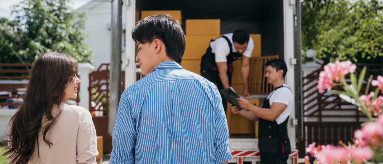 Renter couple watching movers load boxes into a truck after hiring a moving company for their peak-season relocation to a new home.