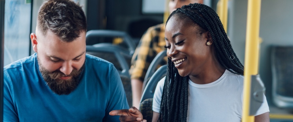 Friends sitting on a bus and using a smartphone while chatting during their ride, showing everyday public transit use in the city.