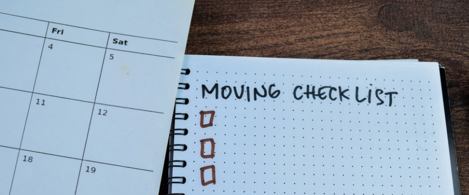 Notebook labeled “Moving Checklist” next to a calendar, representing a renter’s timeline for booking a moving company during peak season.