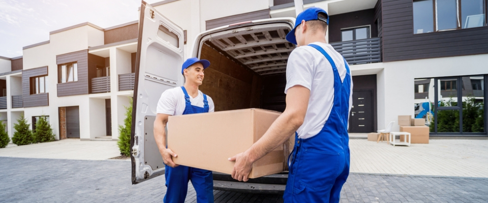 Two movers unloading a large box from a van outside an apartment building, representing a local move handled by a moving company.