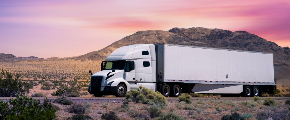 Long-distance moving company truck driving on a highway through a desert landscape at sunset, representing cross-country relocation.