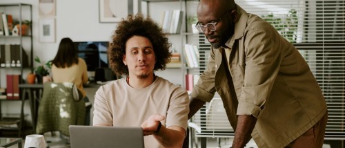 Team leader helping a coworker review documents and discuss details at a desk, illustrating communication and collaboration similar to a co-applicant reviewing an application together.