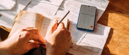 Close-up of hands using a calculator while reviewing utility bills and notes, representing expense tracking and documentation similar to a rent receipt.