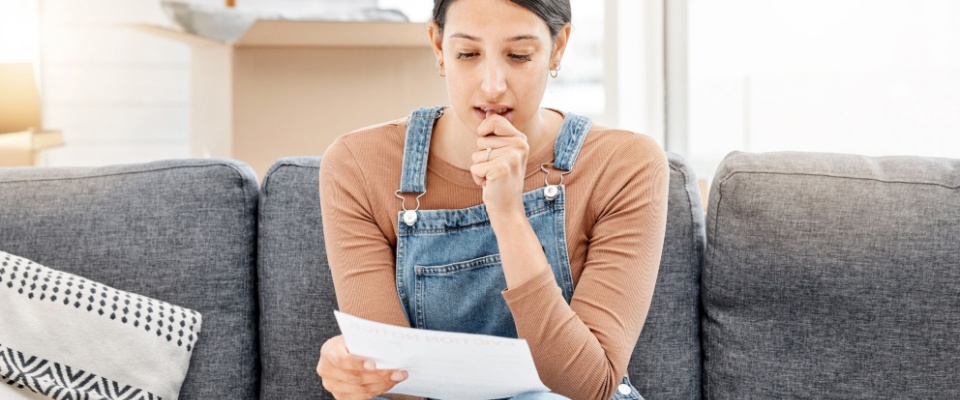 Stressed woman sitting on a sofa surrounded by moving boxes while reviewing paperwork, representing financial concerns and planning a move-in budget during relocation.