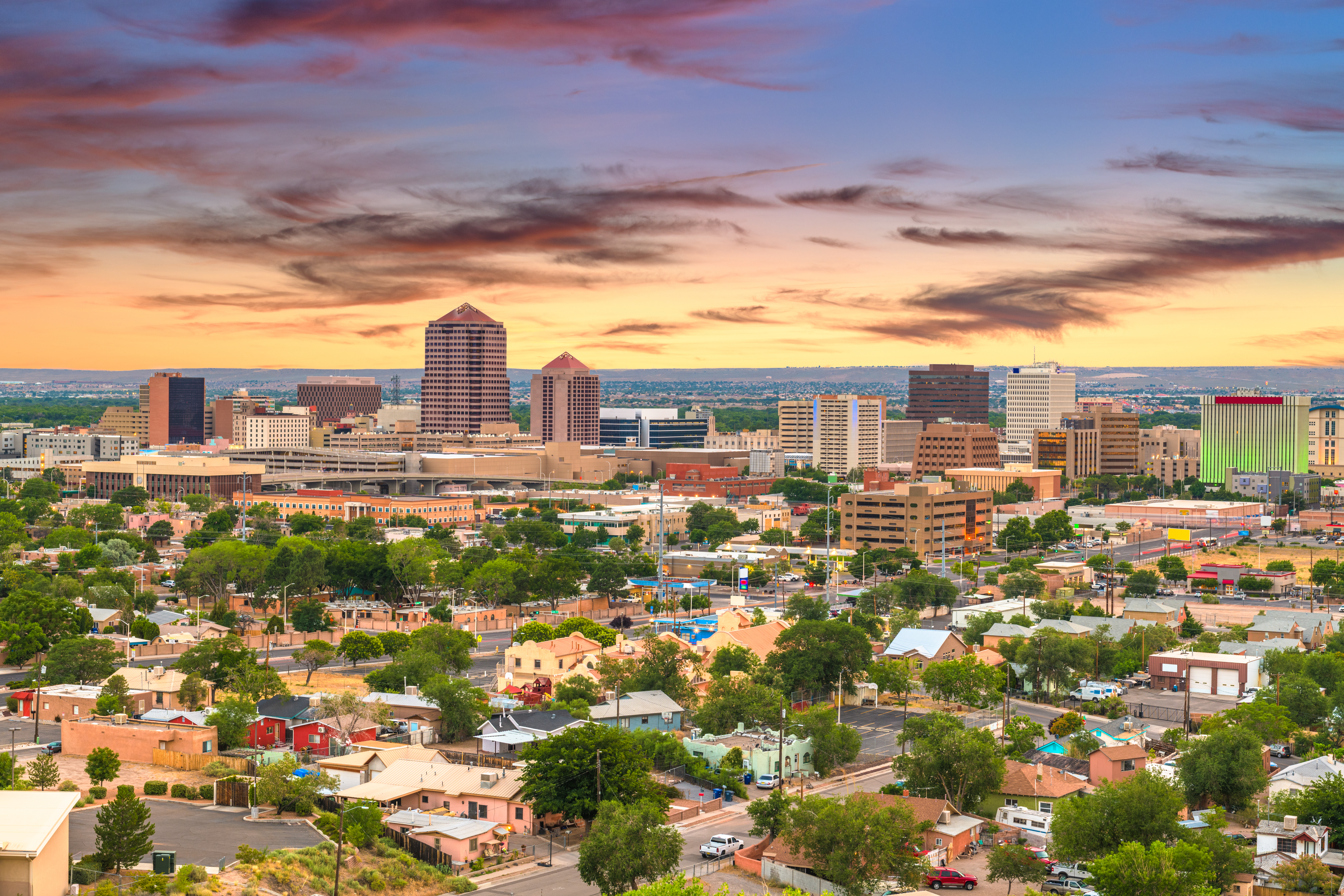 Colorful sunset over downtown skyline and residential neighborhoods, capturing the appeal of renting in Albuquerque, NM.