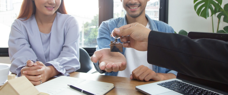 Two people receiving keys from real estate agent after signing lease renewal agreement.