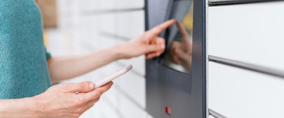A woman's hands holding a smartphone and adding a code on the screen of a smart locker as a key security feature for downtown apartments.