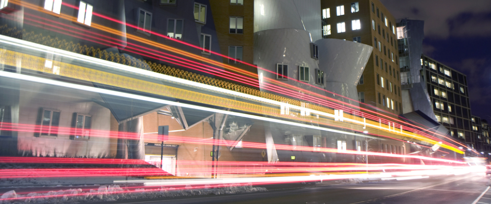 Nighttime street scene with light trails from passing vehicles near modern buildings, illustrating public transit in Cambridge, MA and convenient urban mobility options for renters.