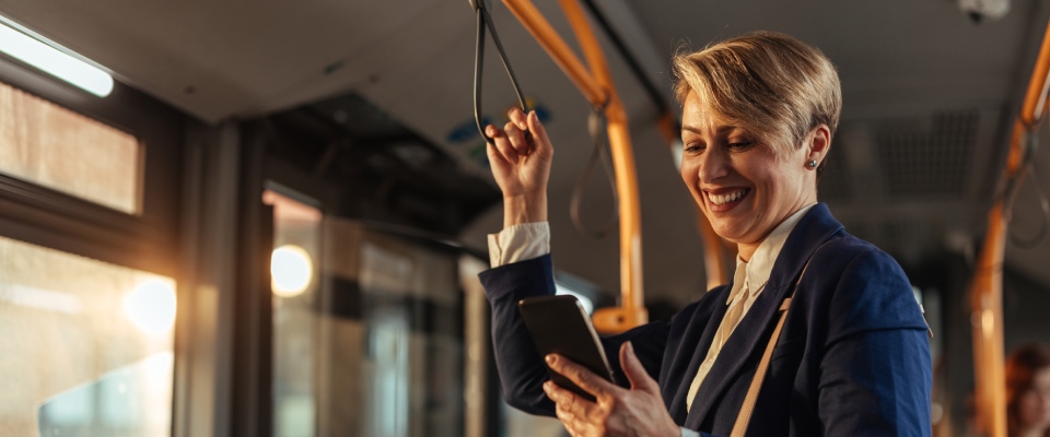 Professional woman smiling while checking her phone on a sunny city bus, illustrating modern commuting and public transit in Hartford.