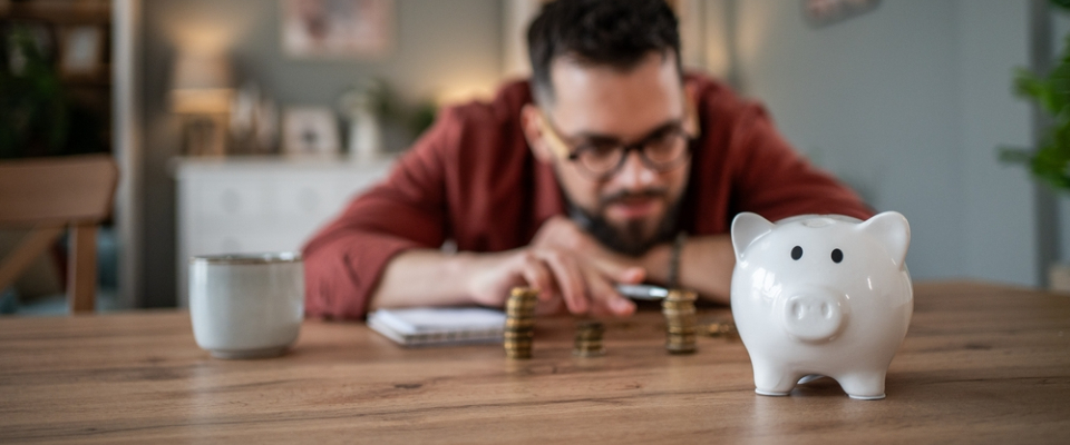 Renter counting coin stacks next to a white piggy bank while evaluating security deposit replacement alternatives to save money on move-in costs.