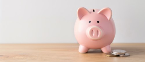 Pink piggy bank with coins on a wooden table representing savings from choosing an Obligo security deposit replacement option for renters.
