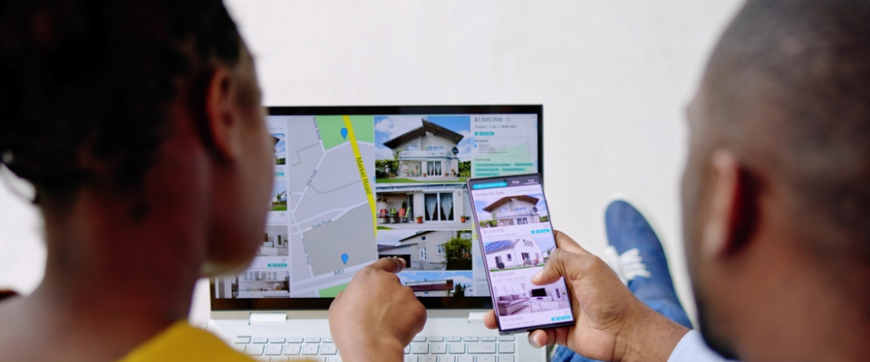 Renters browsing apartment listings on a laptop and phone, comparing options while considering the cost of living.