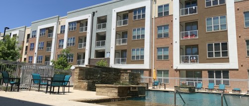 Modern apartment complex in Arlington, TX with a swimming pool, lounge seating, and balconies, showcasing amenities common in affordable neighborhoods for renters.