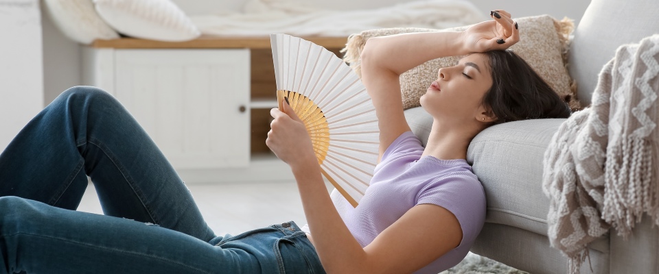 Young woman cooling herself with a hand fan while lying on the living room floor, representing everyday comfort and climate considerations in apartments in El Paso.
