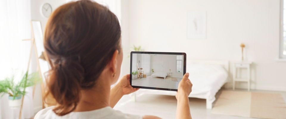 Person exploring a 3D apartment tour on a tablet while standing in a bright, minimally furnished bedroom.