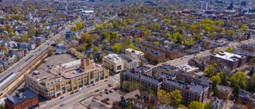 Aerial view of a residential neighborhood with mid-rise buildings, tree-lined streets, and busy roads, highlighting public transit in Cambridge, MA and its accessibility for renters.