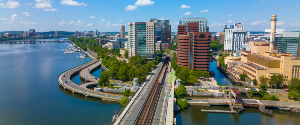 Aerial view of Kendall Square with train tracks, waterfront, and modern buildings, showcasing public transit in Cambridge, MA and easy connectivity for renters.
