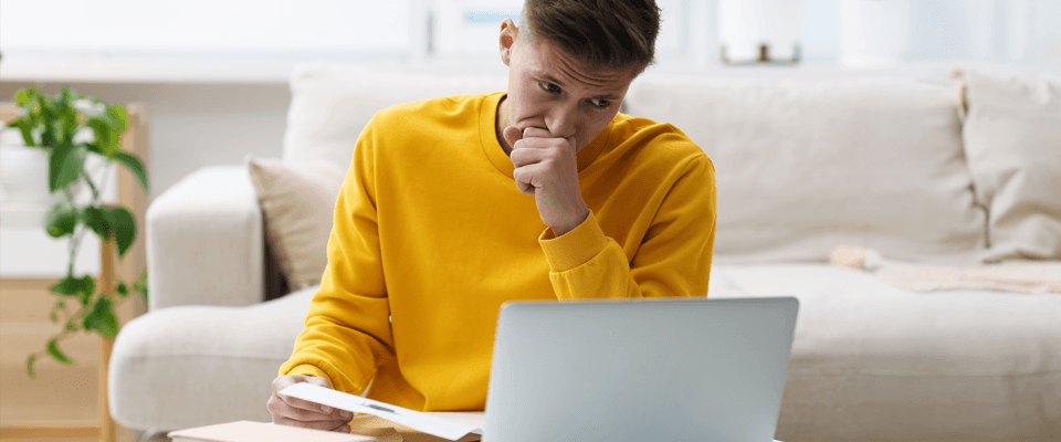 Upset man sitting at a table holding a rejection letter, illustrating the feeling of receiving a rental application rejected notice.