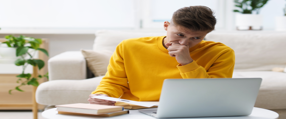 Upset man sitting at a table holding a rejection letter, illustrating the feeling of receiving a rental application rejected notice.
