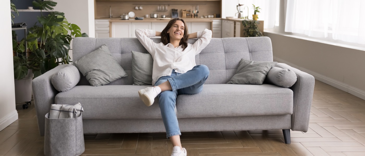 A woman renter smiling and sitting on a couch in an apartment to illustrate making a decision on where to move after making a San Francisco versus Los Angeles cost of living comparison.