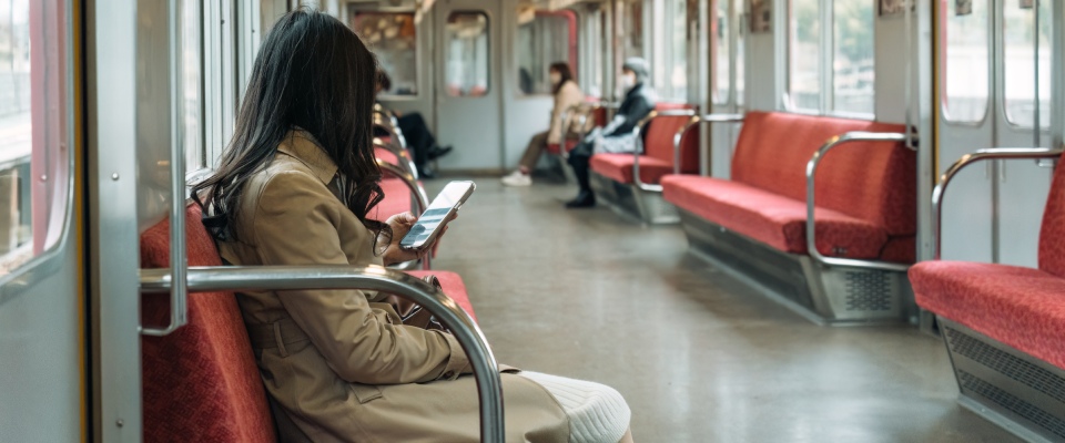 Woman using a mobile phone while riding a city train during her daily commute, illustrating the convenience and accessibility of public transit for everyday travel.