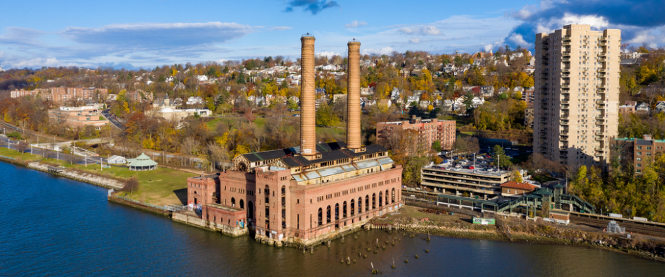 Aerial view of the Yonkers, NY Hudson River shoreline featuring a historic industrial building with twin smokestacks and nearby apartment buildings, underscoring the importance of checking FEMA flood zone maps before renting in Yonkers, NY.