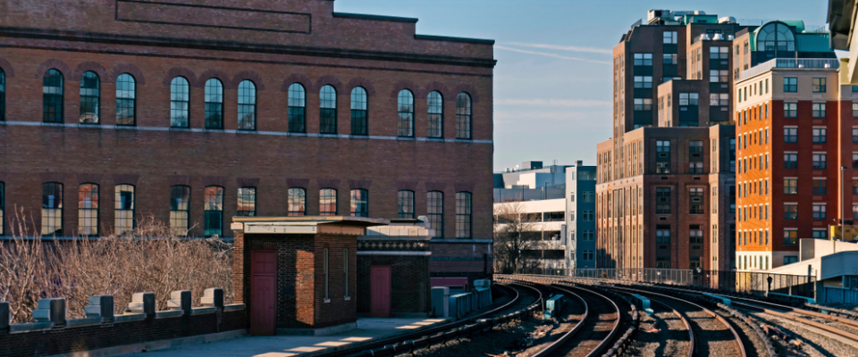 Winter street-level view of Yonkers, NY showing Metro-North railroad tracks curving past historic red-brick buildings and modern apartment towers, capturing the urban character and transit access that define renting in Yonkers, NY.
