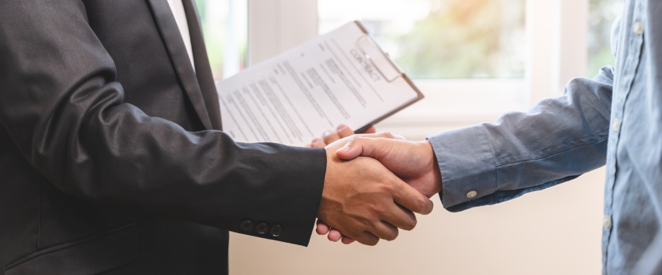 Resident and leasing professional shaking hands after successfully completing a lease agreement, representing lease renewal season and continued residency decisions.