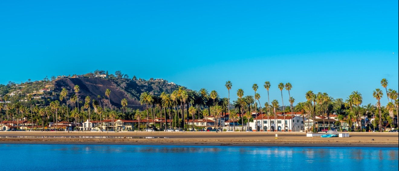 Apartments in Santa Barbara highlighted by a scenic sandy beach lined with palm trees and a clear blue sky, showcasing the area's coastal lifestyle and natural beauty.