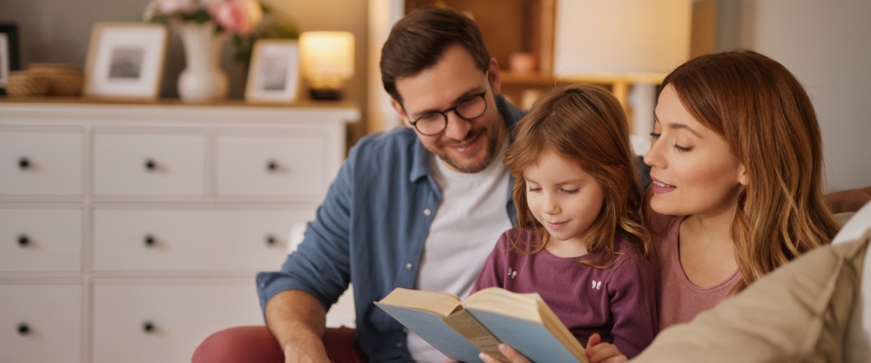 Parents reading a book with their young daughter on a living room sofa, illustrating quality family time and the everyday life of millennial renters with kids.