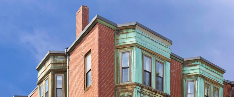 Older Boston brick building with weathered copper bay windows, a reminder to check window insulation when renting in Boston.